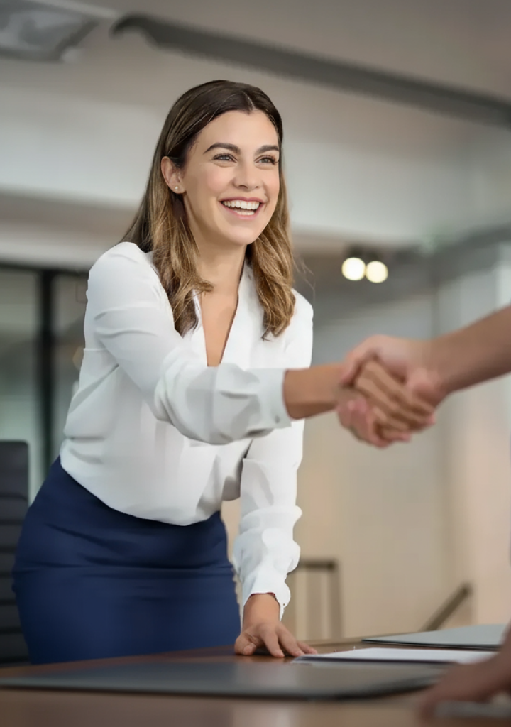 Mujer con atuendo de negocios sonriendo y ofreciendo un apretón de manos.